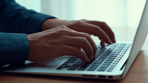 A mão do empresário trabalha em um laptop capaz na mesa do escritório, tiro de perto