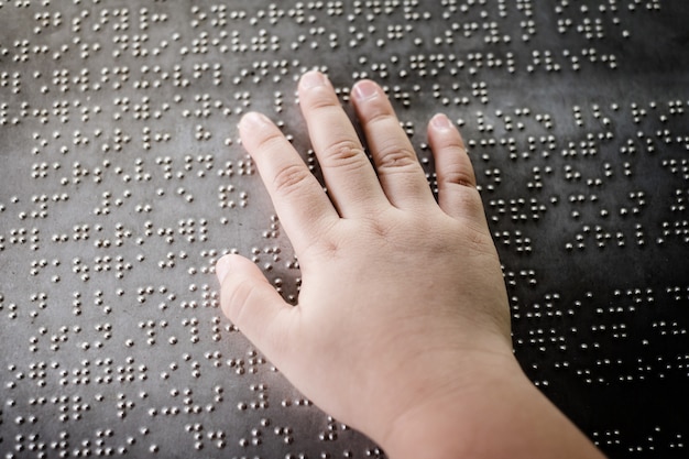 A mão do garoto cego tocando as letras em Braille na placa de metal para entender