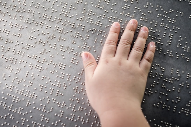 A mão do garoto cego tocando as letras em braille na placa de metal para entender