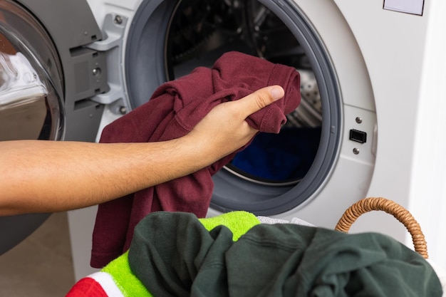 A mão do homem abrindo a frente da máquina de lavar e está prestes a colocar a roupa suja na máquina de lavar