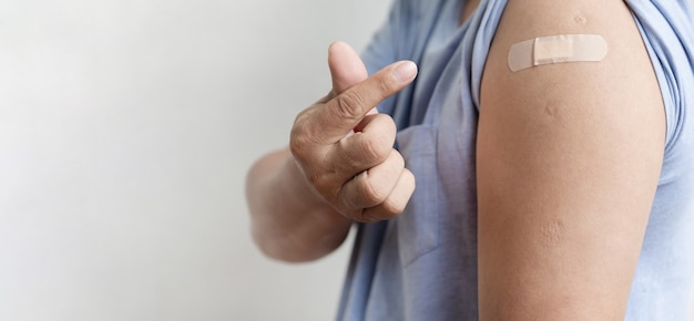 A mão do homem asiático faz um mini coração e mostra o ombro com uma bandagem para vacinar o coronavírus covid