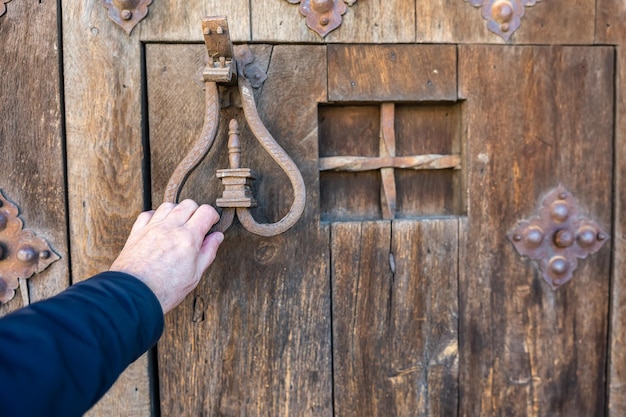 A mão do homem batendo com uma aldrava em uma antiga porta de madeira na cidade medieval de Pedraza Segovia