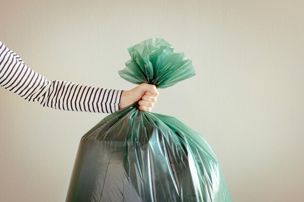 A mão do homem com o saco de lixo verde. fundo neutro.