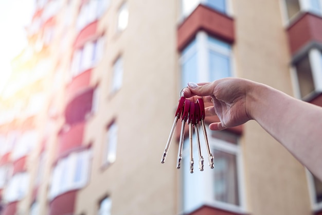 A mão do homem com uma chave e uma casa de chaveiro de metal pendurada do lado no fundo de uma cerca e uma casa de campo Projeto de construção movendo-se para uma nova hipoteca residencial alugando e comprando imóveis