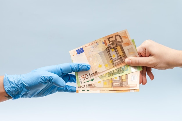 A mão do homem dando dinheiro em euros para uma mão na luva cirúrgica azul, enfermeira ou médico Corrupção na medicina
