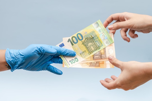 A mão do homem dando dinheiro em euros para uma mão na luva cirúrgica azul, enfermeira ou médico corrupção na medicina