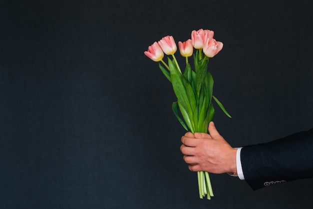 A mão do homem dando um buquê de tulipas cor de rosa