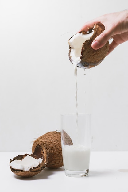 A mão do homem derrama leite de coco em vidro de coco rachado.