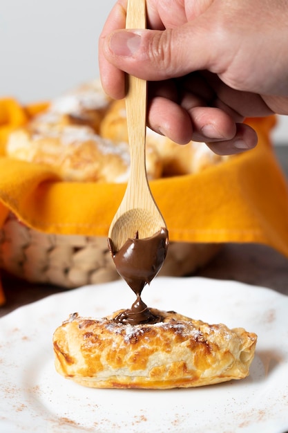 A mão do homem enchendo uma massa folhada com chocolate com uma colher de pau Café da manhã continental