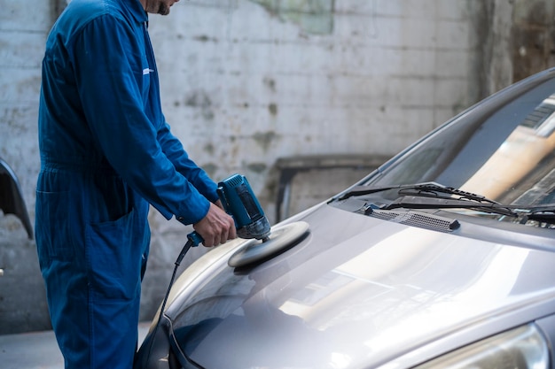 A mão do homem fechado está usando a máquina de polimento de carro na oficina de pintura mecânica