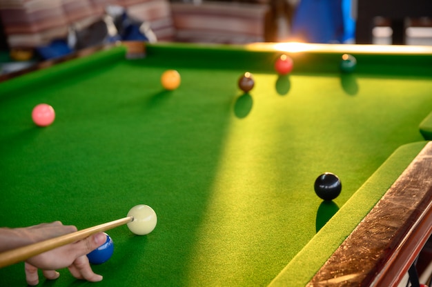 A mão do homem jogando sinuca no bar com bola de sinuca