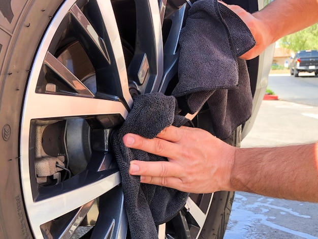 A mão do homem limpando o carro com pano de microfibra preto. Mão limpe a superfície do carro.