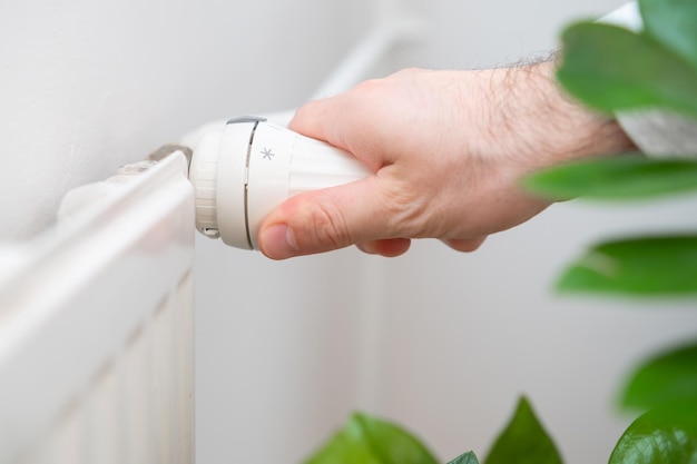 A mão do homem regula o botão de temperatura do radiador de aquecimento para reduzir os custos de aquecimento