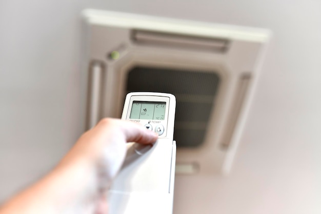 A mão do homem regulando o ar condicionado a 27 graus devido à crise energética Ar condicionado ou bomba de calor