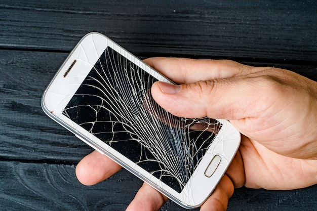 Foto a mão do homem segura o telefone móvel com touchscreen quebrado em fundo escuro