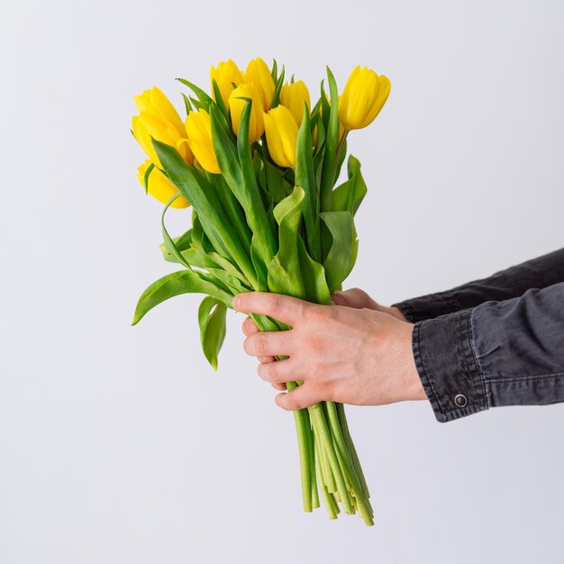 A mão do homem segura um buquê de tulipas amarelas, símbolo de amor.