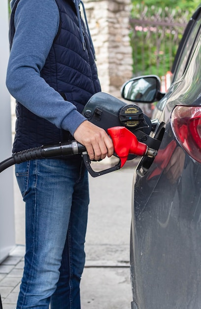 A mão do homem segura uma bomba de combustível vermelha para reabastecer seu carro preto no posto de gasolina