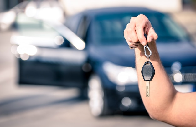 A mão do homem segurando as chaves do carro moderno prontos para locação