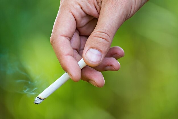 A mão do homem segurando um cigarro aceso