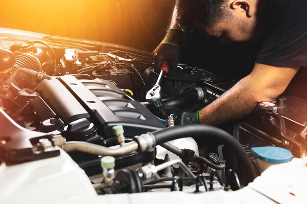 A mão do mecânico usando luvas pretas é apertar o parafuso com a chave de caixa para consertar o motor do carro