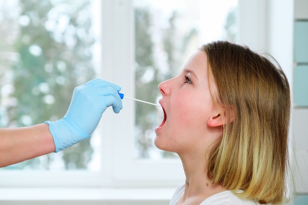 A mão do médico com um cotonete tira uma análise da boca de uma menina.