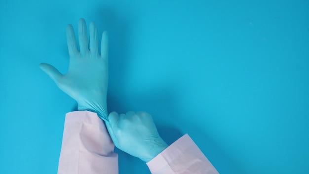 Foto a mão do médico está puxando luvas de látex azuis sobre fundo azul