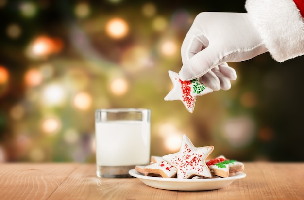 A mão do papai noel tira biscoitos de um prato no fundo de uma árvore de natal