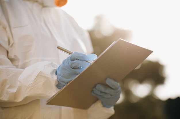 Foto a mão do virologista em uma luva branca segura uma caneta em uma folha de papel em branco. o médico segurando a prancheta com papel em branco na mão