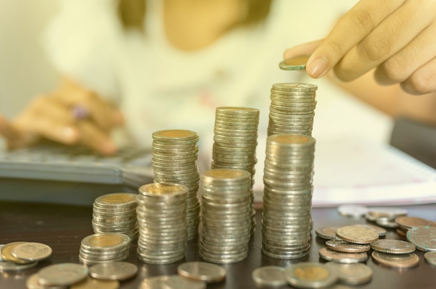 A mão está colocando moedas e moedas acumuladas em coluna que representam economia de dinheiro ou ideia de planejamento financeiro para a economia.