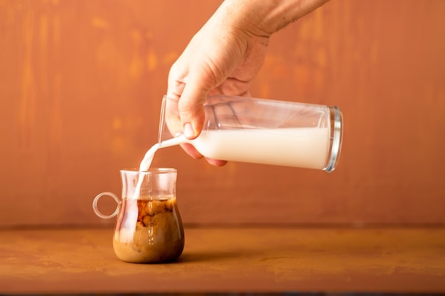 A mão está derramando leite no café em estúdio com espaço de cópia