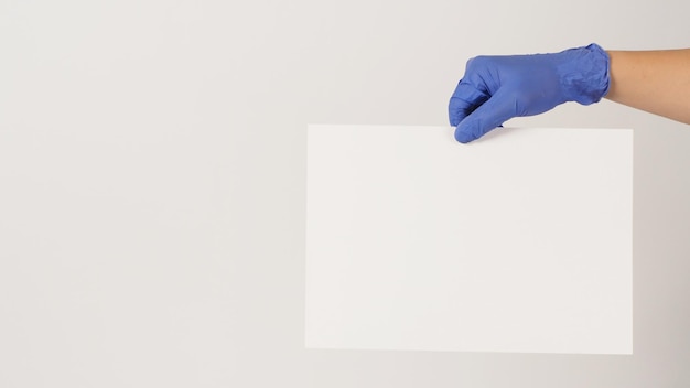 A mão está segurando o papel A4 e usa luva de látex roxa sobre fundo branco