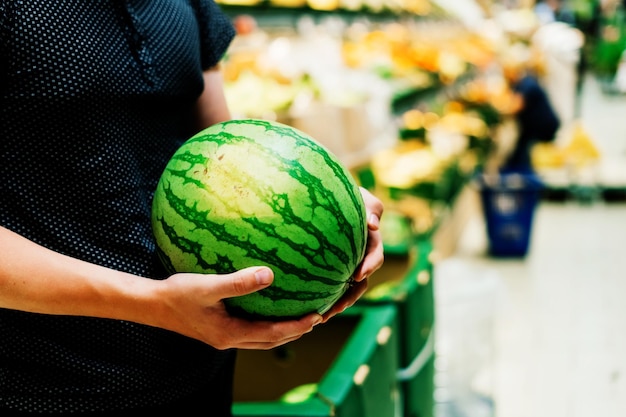 A mão está segurando uma melancia da prateleira do supermercado em close-up