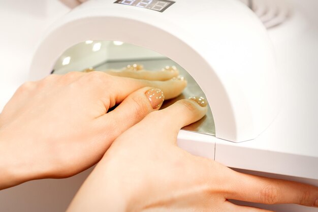 A mão feminina com os dedos bem cuidados seque dentro da máquina de luz UV no salão de manicure.