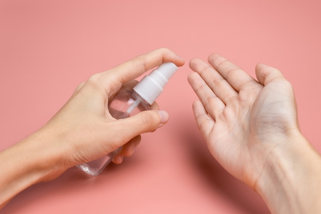 A mão feminina com um anti-séptico aplica um líquido na palma da mão em um close-up de fundo rosa. O conceito de higiene e limpeza. Desinfetante