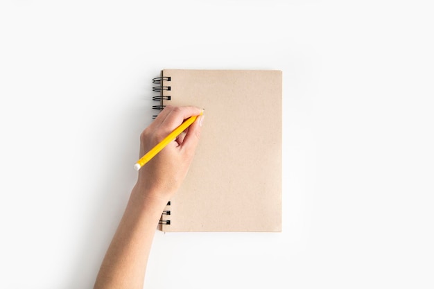 A mão feminina escreve com um lápis em um notebook em um fundo branco