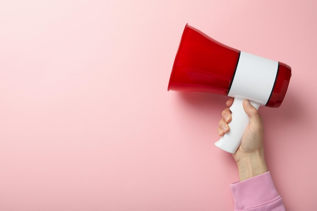 A mão feminina segura o megafone no fundo rosa