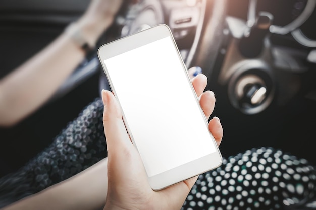 A mão feminina segura um telefone celular com uma tela branca em branco no espaço de cópia da maquete do interior do carro