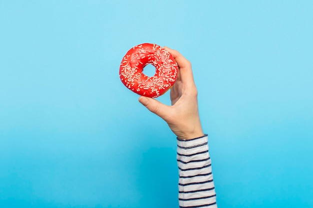 A mão feminina segura uma rosquinha em um fundo azul Conceito confeitaria pastelaria cafeteria Banner Flat lay top view