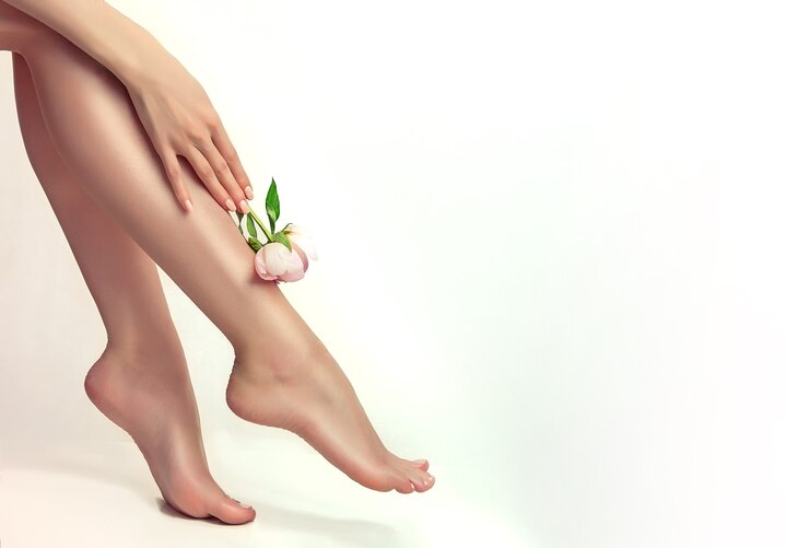 A mão graciosa de uma mulher segurando uma flor de peônia e tocando uma perna bem cuidada. Beleza e cuidados com o corpo