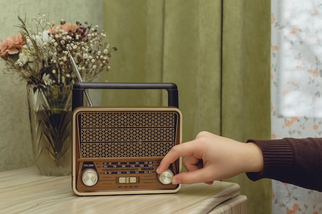 A mão liga o rádio de pé na sala na cômoda ao lado do vaso de flores