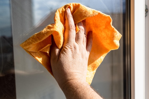 A mão masculina limpa a superfície do vidro de janela com pano