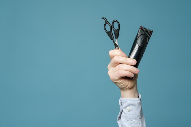 A mão masculina segura uma tesoura de cabeleireiro e um aparador sem fio