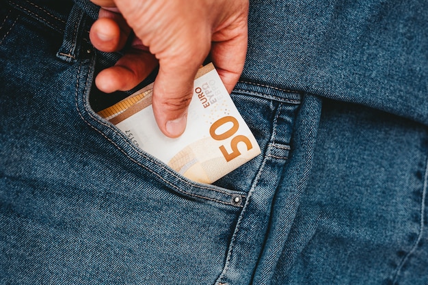 A mão que coloca notas de euro em um bolso de jeans