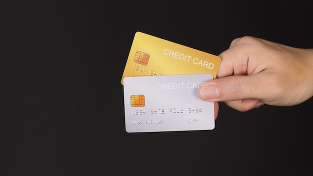A mão segura dois cartões de crédito Cartões de crédito dourados e prateados isolados em fundo preto