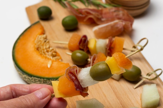 A mão segura o espeto com azeitonas de queijo e presunto Melon jamon e azeitonas a bordo