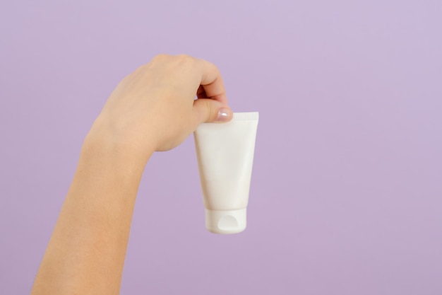 A mão segura o tubo branco plástico isolado no fundo lilás Conceito de beleza Tubo de embalagem para produtos cosméticos