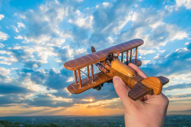 A mão segura um avião de madeira no fundo de um céu