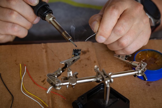 A mão segurando a lata um ferro de solda solda o chip no lugar um homem solda um fio a um microcircuito