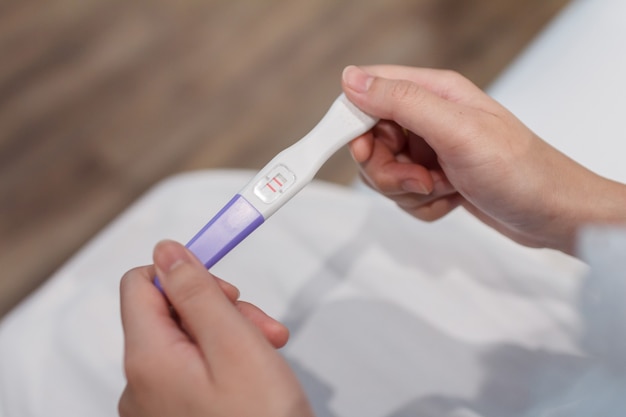Foto a mão segurando o teste de gravidez está mostrando um resultado positivo.
