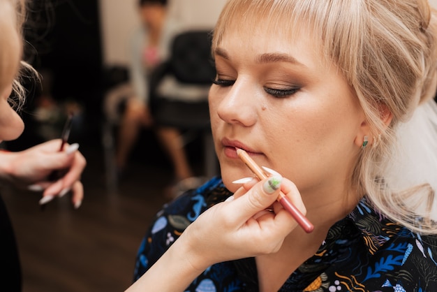 A maquiadora usa um lápis labial para pintar os lábios da modelo com uma cor suave.
